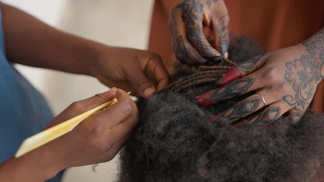Intricate braid styling black client with tattooed hands, closeup of textured afro and long painted nails, fingers weaving small sections with precise rhythm, intimate artistic grooming scene