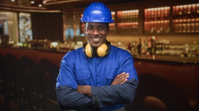 Man construction worker wearing blue hardhat and yellow earmuffs, arms crossed and smiling in building; confidence.