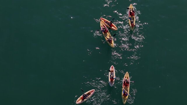 Aerial view of multiple kayakers paddling in the deep teal waters, creating ripples as they navigate the serene sea, Cascais, Lisbon, Portugal.