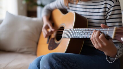 Fototapeta premium Close-up of person practicing acoustic guitar on sofa at home.