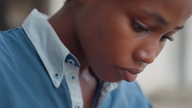 Closeup black apprentice studying wood grain, focused profile shot of young woodworker inspecting board, subtle expression of concentration, denim shirt, headwrap, workshop background blurred, hands