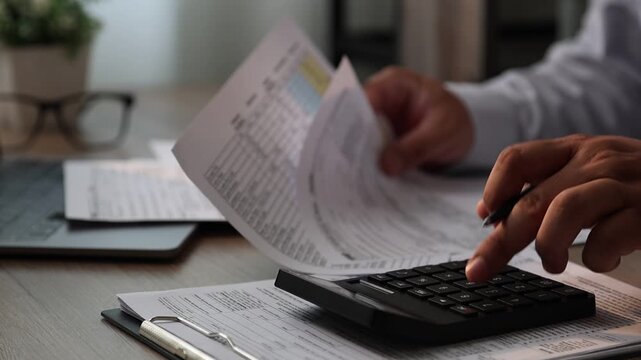 Close-up of a person organizing receipts and calculating expenses with a calculator while writing on financial documents at a desk with a laptop, suitable for expense tracking, budgeting, reimbursemen