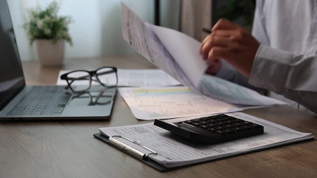 Close-up of a person organizing receipts and calculating expenses with a calculator while writing on financial documents at a desk with a laptop, suitable for expense tracking, budgeting, reimbursemen