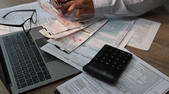 Close-up of a person organizing receipts and calculating expenses with a calculator while writing on financial documents at a desk with a laptop, suitable for expense tracking, budgeting, reimbursemen