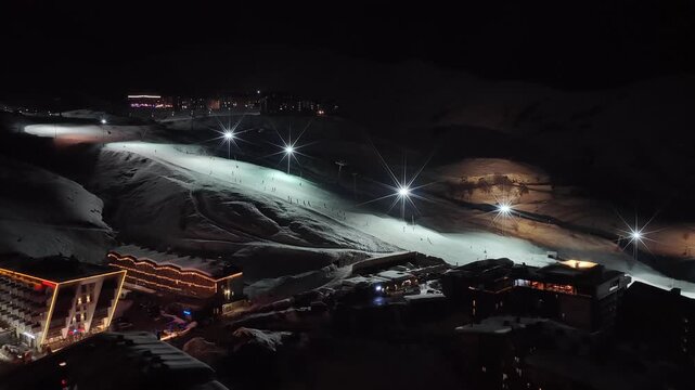 Night Drone view of Gudauri in Georgia town with snow covered mountains, ski slopes and town after fresh snowfall in winter season. Gudauri ski resort with fresh powder snow, Georgia.