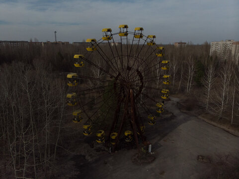 Aerial view of the abandoned Ferris wheel with yellow cabins surrounded by leafless trees and distant apartment blocks in Pripyat, Kyiv Oblast, Ukraine.