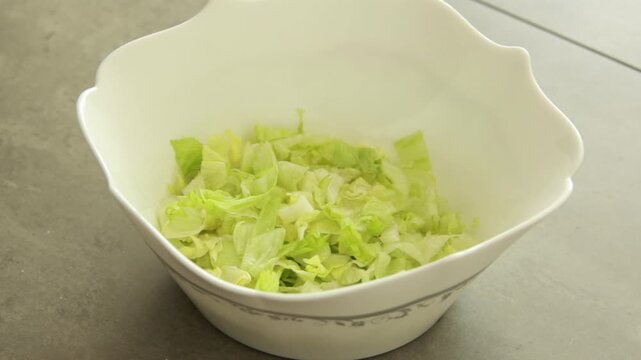 Fresh chopped iceberg lettuce falling into a salad bowl, close up slow motion food preparation