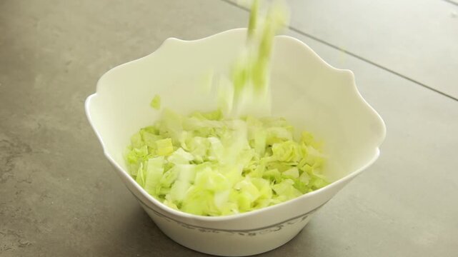 Fresh chopped iceberg lettuce falling into a salad bowl, close up slow motion food preparation