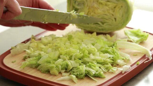 Chopping fresh iceberg lettuce on wooden cutting board, close up of healthy salad preparation on light background