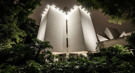 Fototapeta premium Striking Brutalist Concrete Building at Night with Dramatic Lighting and Lush Greenery