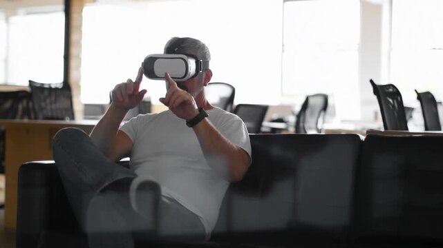Tech worker seated on sofa with VR HMD testing VR interface on red particles appearing, fading