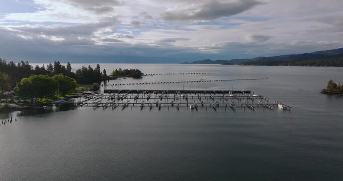 Long empty dock extending across calm lake water toward distant shoreline under soft cloudy sky, Flathead Lake Montana USA