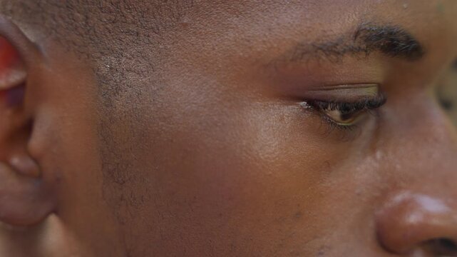 Close up profile black man contemplative gaze, soft natural lighting reveals skin texture and quiet sheen, eyes lowered in focused reflection, slight jaw tension and subtle expression conveying
