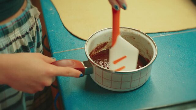 Close up of teenage hands using a spatula to spread a mixture of cinnamon, sugar, and butter on rolled out dough. Rich texture of sweet filling for traditional cinnamon buns.
