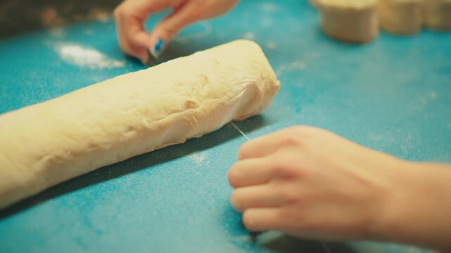 Close up of teenage hands using a knife to slice the dough log into individual cinnamon rolls. Perfect spiral cross-section of raw yeast pastry before baking.