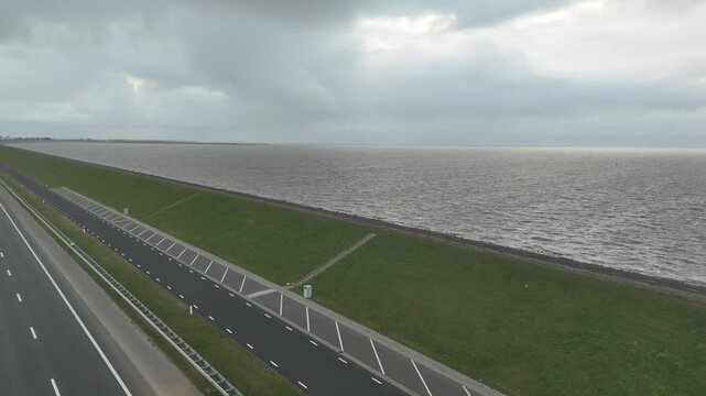 Slow aerial view across dam and open sea with bus