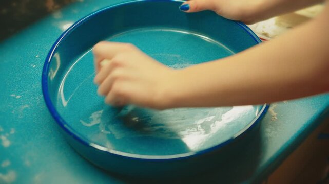 Close up of teenage hands greasing a round baking dish with butter to prevent sticking. Essential preparation step for baking homemade sweet rolls.