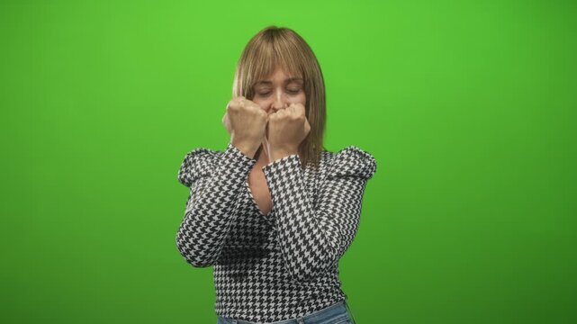 Woman with clenched fists punching toward camera in studio, wearing houndstooth blouse and jeans against a green screen backdrop; confidence.