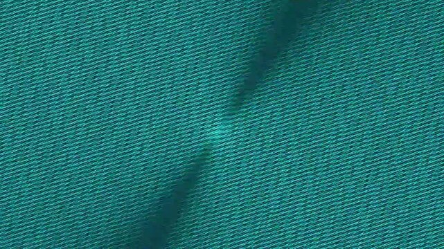 Close up shot reveals the detailed woven texture and deep teal color of a dense fabric surface featuring a subtle diagonal crease or fold element in the center.