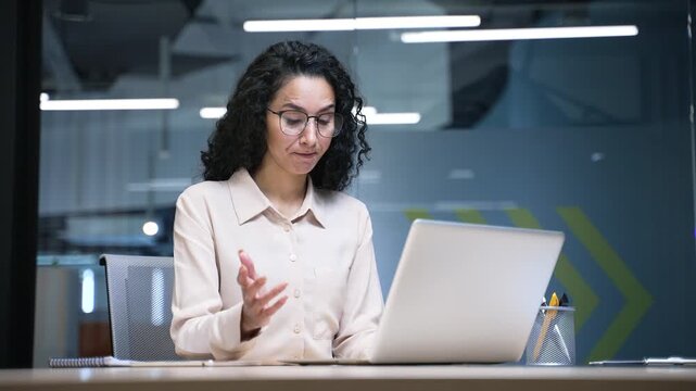 Frustrated businesswoman complains about poor performance of software on laptop sitting at desk at workplace in business office. Woman is dissatisfied with work of computer, Internet or service