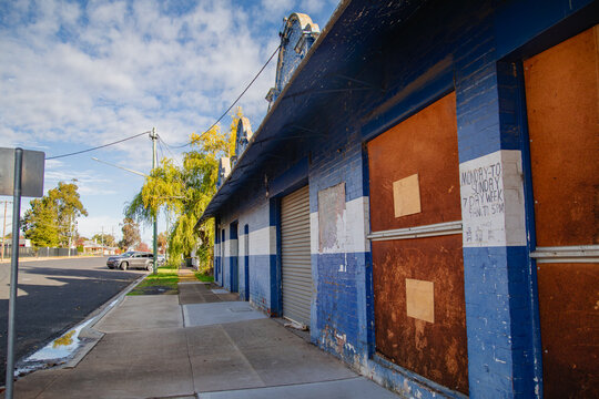 Abandoned blue and white brick building with boarded-up windows on a sunny day