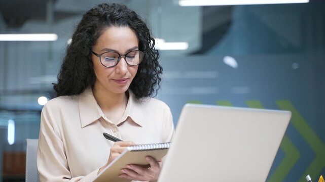 Businesswoman watching video call online conference taking notes looking at laptop screen sitting in office. Female employee listening business training communicates in a remote meeting. Close up