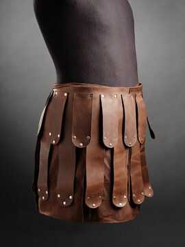 Brown leather skirt armor with layered riveted panels on mannequin side view.
