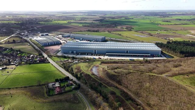 Aerial view of distribution center with rows of delivery trucks and lush green fields, contrasting with brown vegetation, Doncaster, England, United Kingdom.