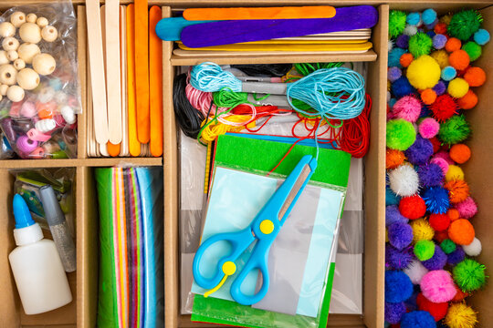 Colorful craft supplies kit with scissors paper threads beads and pom poms arranged in box on table. Creativity development fine motor skills and kids education concept.