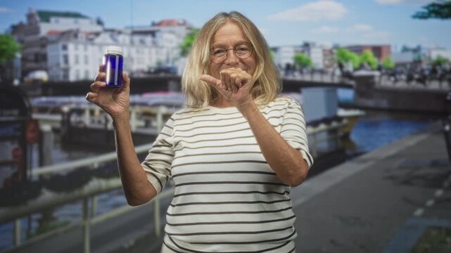 Woman holds blue pill bottle in left hand while showing a small gap with thumb and forefinger on a street; health confidence.