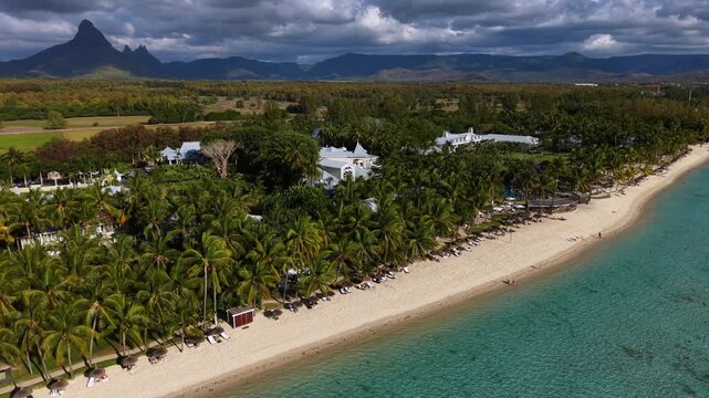 Keyframe 1 Aerial view of a pristine beach. Turquoise water laps the shore. White sand stretches wide. Palm trees grow along the coast. White buildings blend with nature