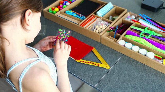 Little girl decorating handmade craft with colorful self adhesive rhinestones at table. Kids creativity fine motor skills development and learning through play concept.