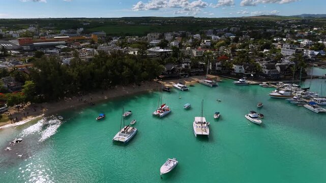 Harbor waters glow turquoise with numerous boats. Aerial view shows lush greenery and a coastal town. Gentle waves lap against golden sand beaches. Perfect for travel, vacation