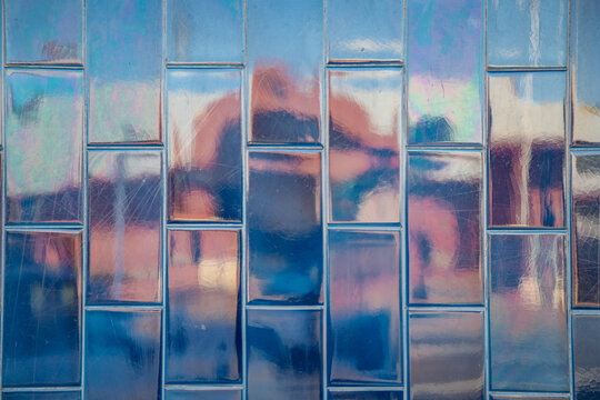 Iridescent blue rectangular tiles with reflections of warm colours and sky