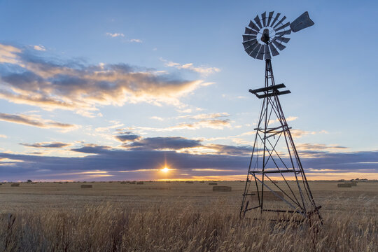 Looking up at a farm windmill in paddock against a sunset sky