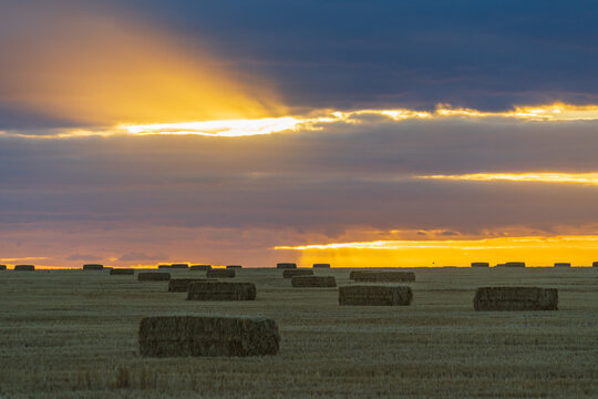 Dramatic rays of light through a gap in the clouds at sunset over hay bales in a paddock