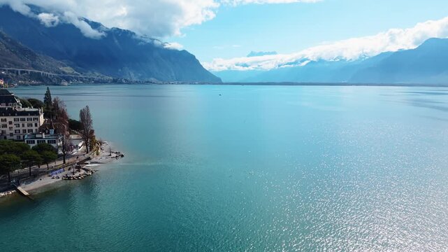 Aerial view of the serene waters meeting the land near Montreux, with the majestic Dents du Midi mountains cloaked in clouds, Vaud, Switzerland.