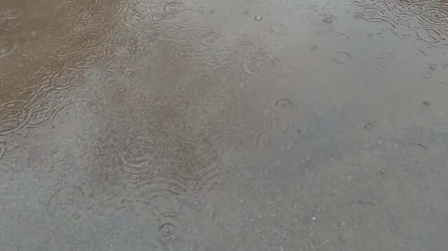 Slow motion of rain drops falling into a puddle on the sidewalk. Flooded sidewalk during heavy rain. 