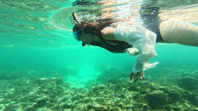 Woman in swimsuit and shirt snorkeling over reef in turquoise tropical water