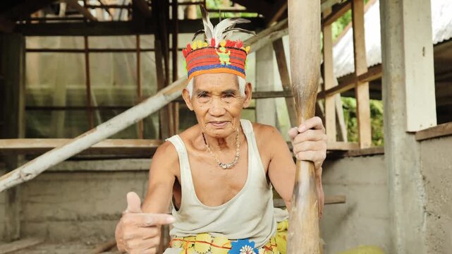 Filipino farmer facing camera holding wooden pestle and pointing gesture
