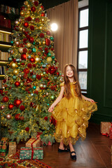 Child in yellow dress stands by a decorated Christmas tree with gifts