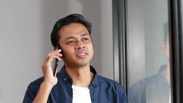 Asian man smiling with phone call for talking, gossip and communication with digital contact near window at home