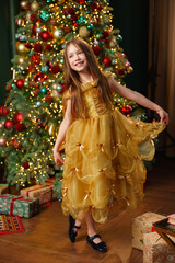 Young girl in yellow dress smiles near Christmas tree with gifts