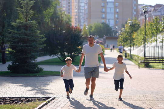 A joyful scene of a father spending quality time walking with his two sons in a green city park on a sunny day, showcasing family values, leisure, and the enjoyment of outdoor activities.