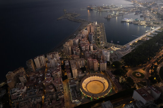 Aerial view of the illuminated Plaza de toros de La Malagueta bullring and the city skyline at night in Malaga, Andalusia, Spain.