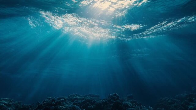 Submerged view of the deep ocean, sunlight piercing through waves with coral reef below