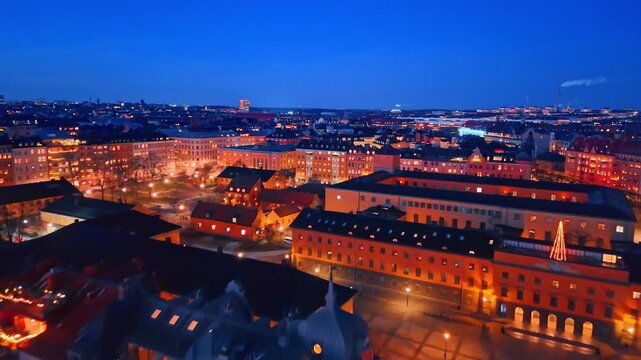 Night aerial view of illuminated brick buildings and city square. High angle shot of red brick architecture at night with warm window lights and glowing street lamps in Stockholm.