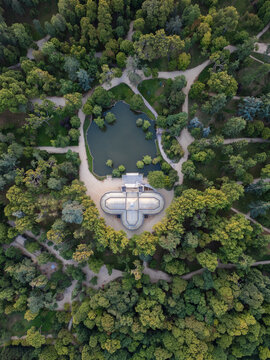 Aerial view of the Palacio de Cristal and its pond surrounded by lush green trees and winding paths in Retiro Park, Madrid, Community of Madrid, Spain.