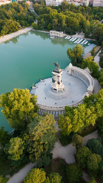 Aerial view of the Monument to Alfonso XII and the Retiro Park Lake surrounded by lush green trees in Madrid, Community of Madrid, Spain.