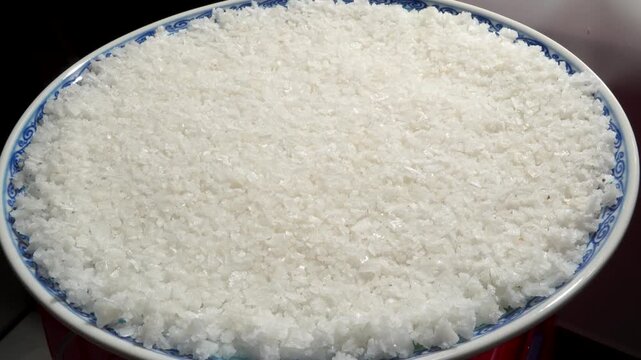 Macro rotating view of coarse white sea salt on a patterned ceramic plate. Pure natural mineral texture for healthy culinary and food preparation.